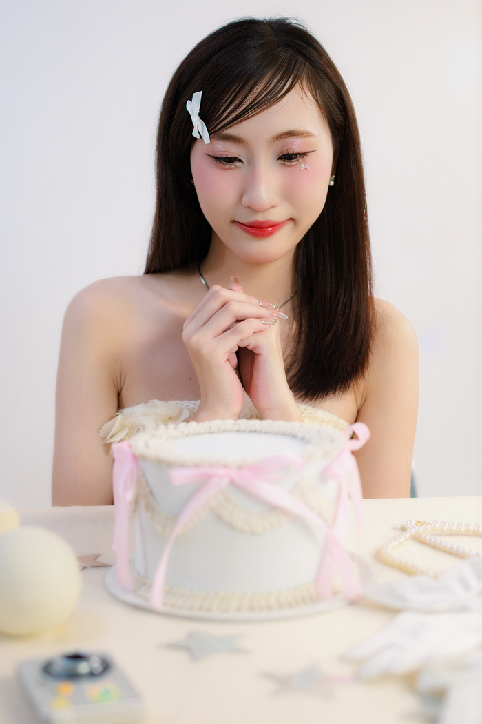 Smiling young woman with a cake, enjoying a special occasion indoors. Light pastel setup.
